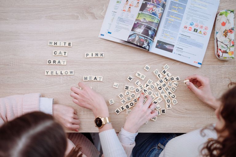 Grupa znajomych grająca w scrabble i czytająca podręcznik