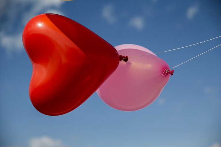 Czerwony balon w kształcie serca i różowy balon obok niego unoszące się na błękitnym niebie